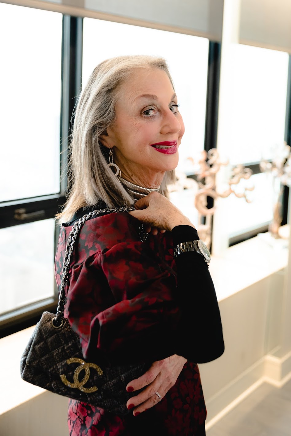 Woman (Honey Good) with Gray Hair smiling and holding Chanel bag over shoulder. 