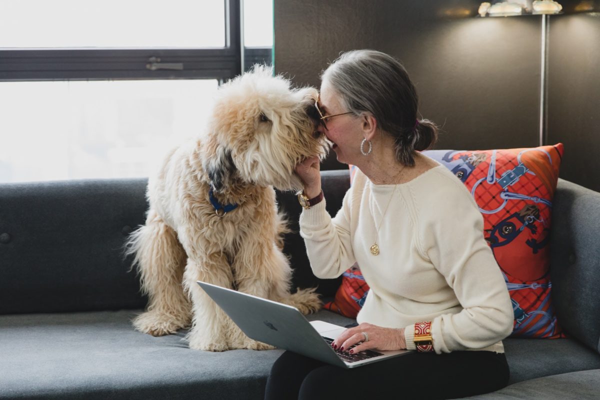 Woman (Honey Good) and her dog on sofa smiling while being licked.