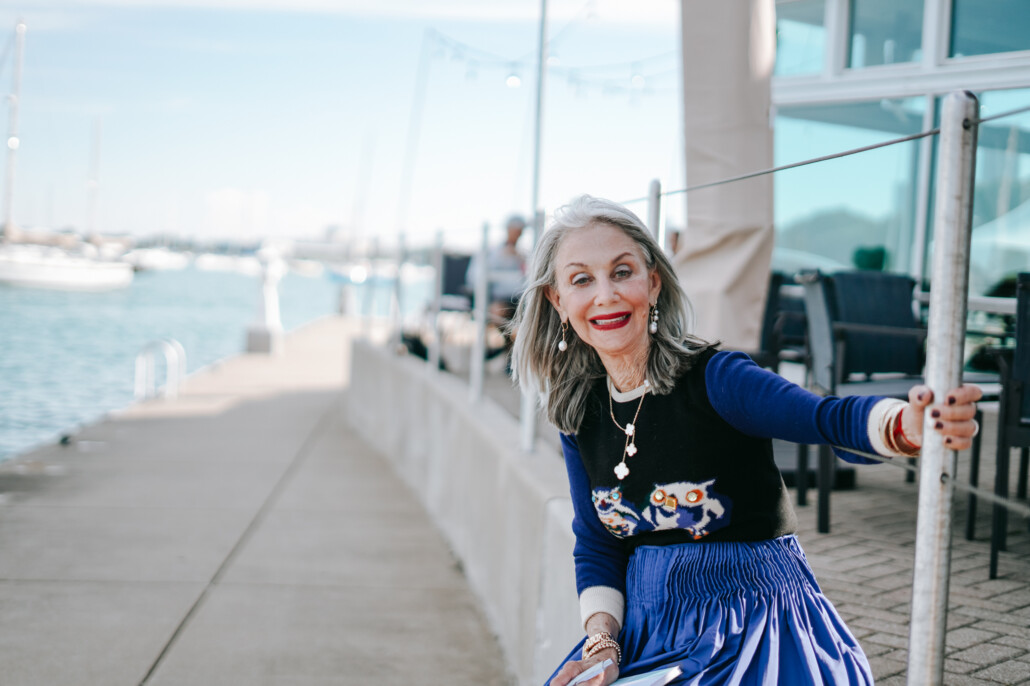 Honey Good in blue skirt and sweater, leaning by concrete railing at the waterfront in Chicago learning to bloom where planted.