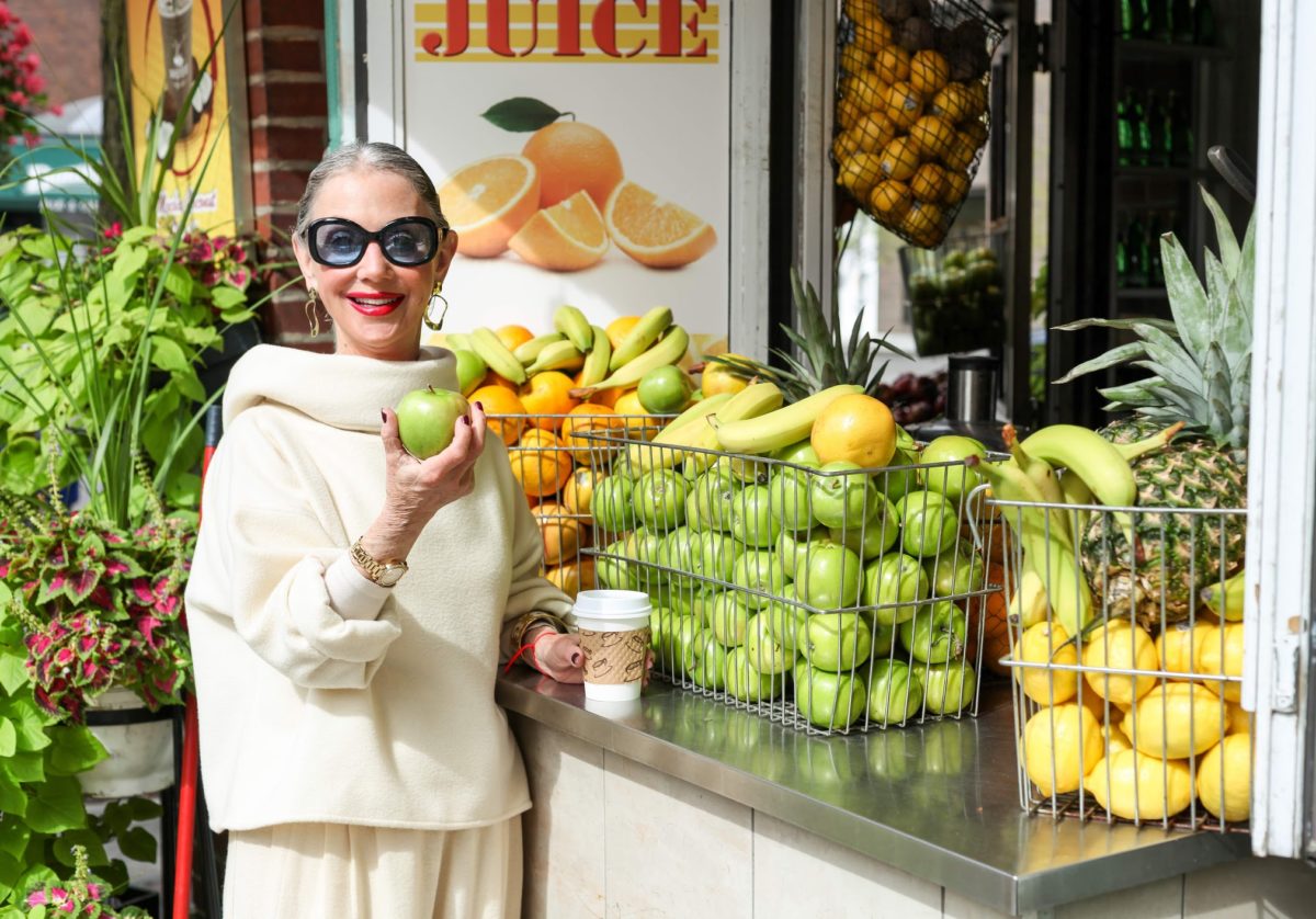 image of seasonal foods to try this winter with Honey Good in front of a fruit stand holding a green apple.