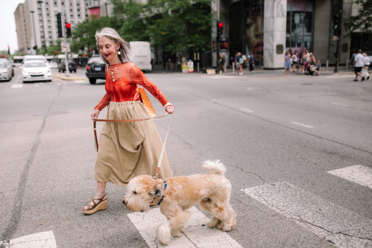 Smiling, Grey-Haired Woman (Honey Good) Walking dog across the street.