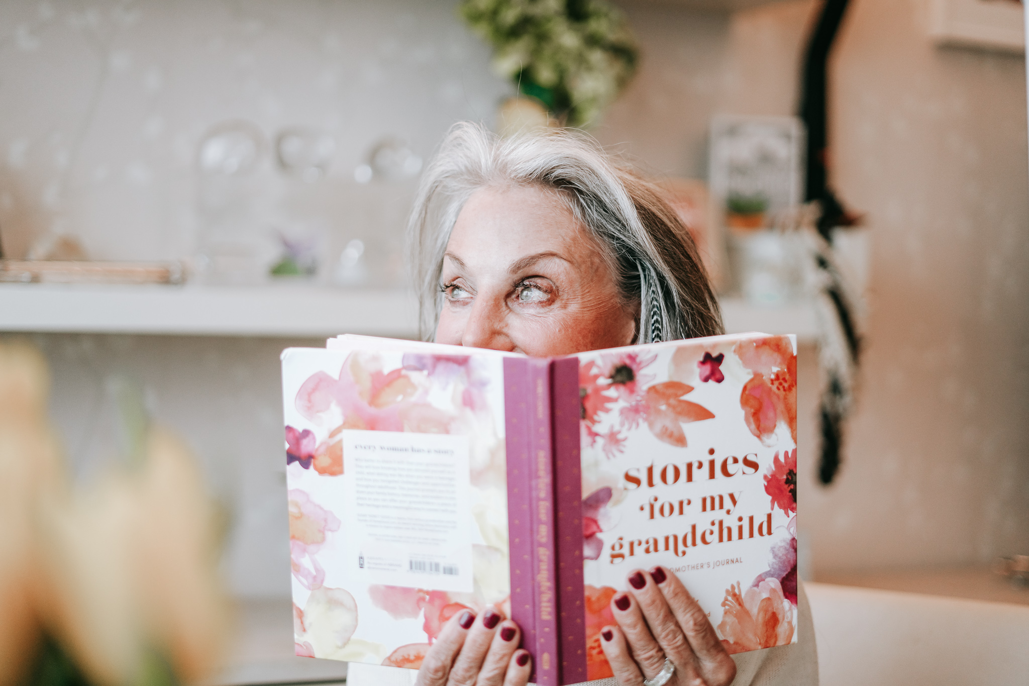 image of honey good holding up her book, Stories for My Grandchildren" in front of her face up to her eyes. She shares her stories and her wisdom of how to avoid grandparent mistakes