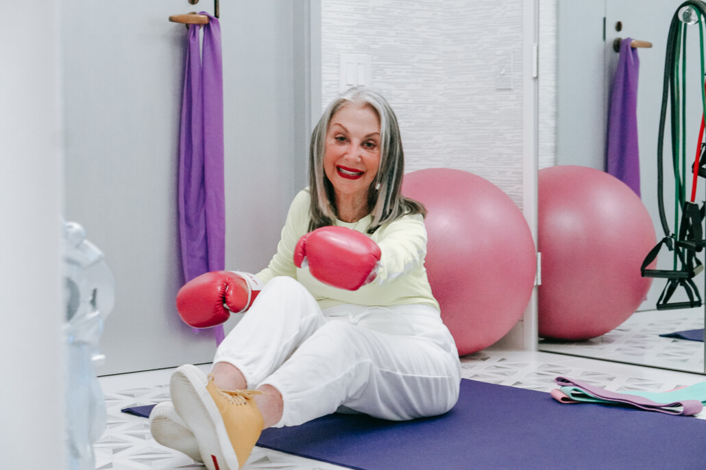 Honey good sitting on yoga mat donning pink boxing gloves fighting for positive aging and body positivity
