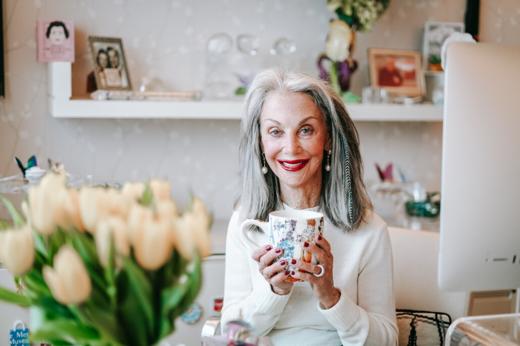 Honey Good holds a coffee cup sitting at desk with computer, peace of mind after 50