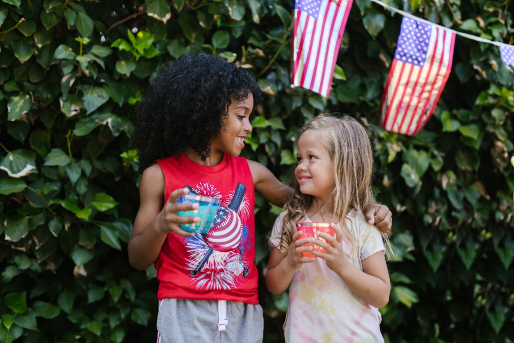 two girls in red white and blue smiling at eachother hearing 4th of july jokes for kids.