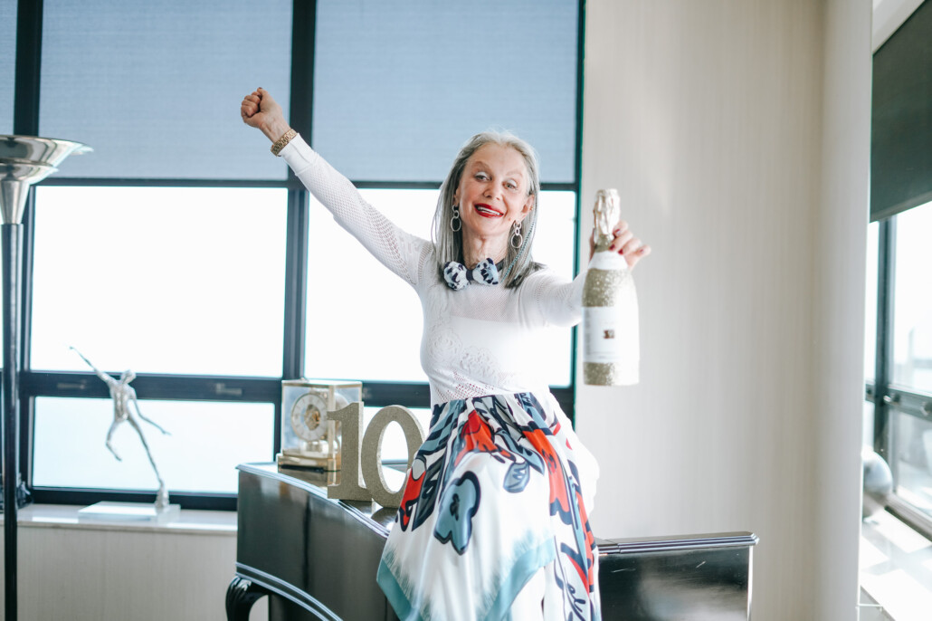 Image of honey good as a woman over 50 dressed for a holiday party and ready to celebrate with a bottle of champagne.